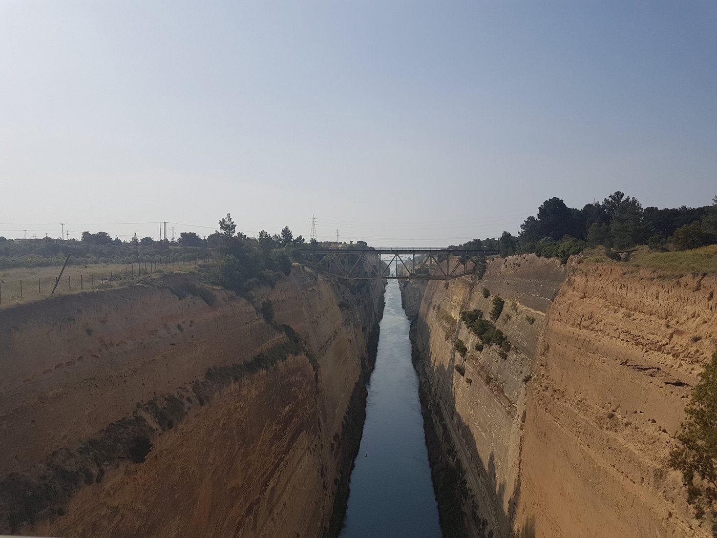 The Corinth Canal cutting a narrow straight channel between towering rock walls, seen from the bridge