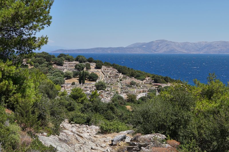 Ancient stone walls and ruins of the fortified settlement at Rhamnous, with wild vegetation and a view toward the coast of Attica