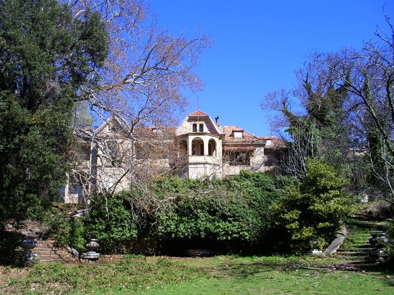 The neoclassical Tatoi Palace seen from the royal gardens, partially obscured by surrounding greenery