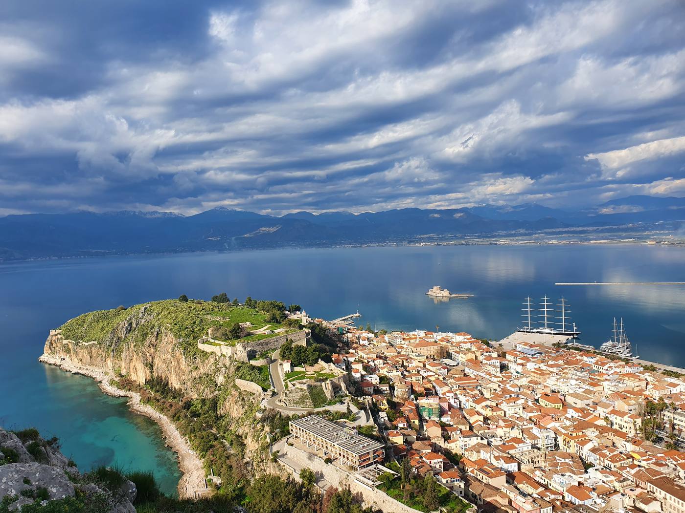View down from Palamidi fortress over the red-roofed old town of Nafplio, with the small island castle of Bourtzi in the bay and mountains across the gulf