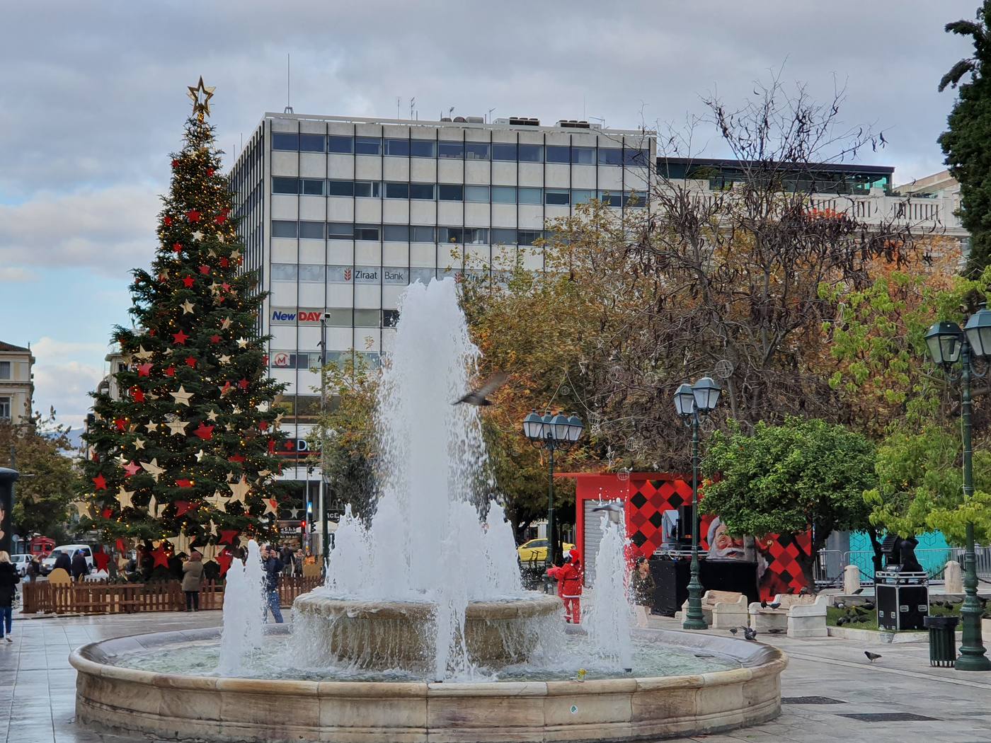 People in winter coats around the fountain in Syntagma Square under a grey December sky
